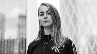 Black and white photo of DJ ELEANOR standing in front of two tall buildings