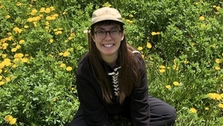 Photo of DJ Pacifier sitting cross-legged on the grass and wearing a hat