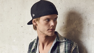 Avicii leaning against a wall with a backwards dark baseball cap