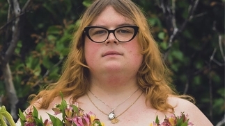 Photo of Baby Weight holding a bouquet of flowers and wearing black thick-rimmed glasses