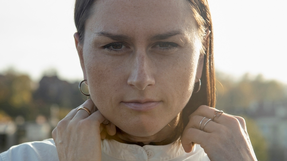 Photo of Polish producer Olivia looking into the camera while touching the collar of her cream coat