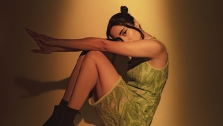 Photo of SUCHI wearing a green dress under a yellow spotlight.