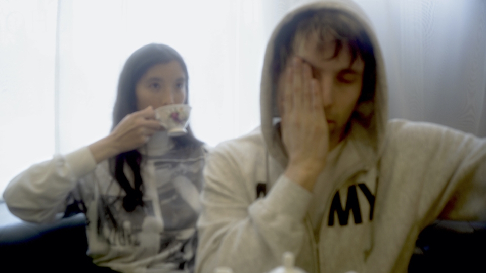 Photo of DJ Python touching his face and Ana Roxanne drinking from a mug.