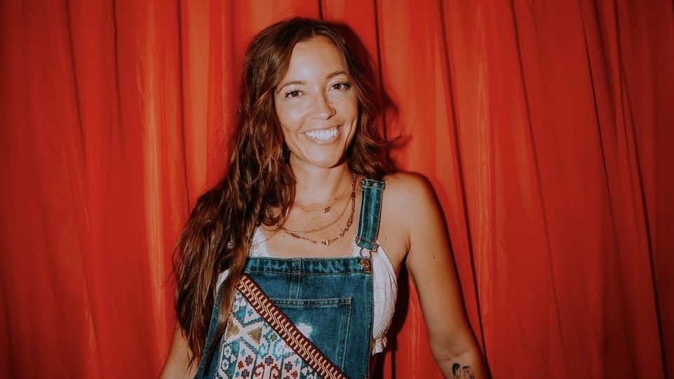 Photo of LP Giobbi wearing dungarees in front of a red curtain