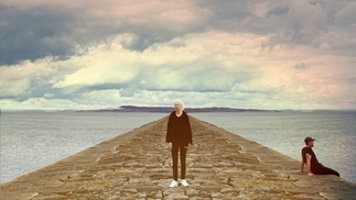 Photo of Lord Of The Isles and Ellen Renten standing on a pier in front of a rainbow sky