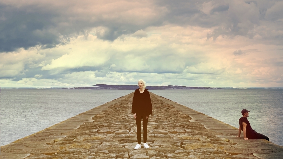 Photo of Lord Of The Isles and Ellen Renten standing on a pier in front of a rainbow sky