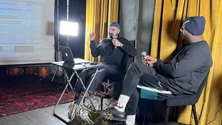 Photo of Moving Still and Tony Nwachukwu recording a workshop in front of a yellow curtain