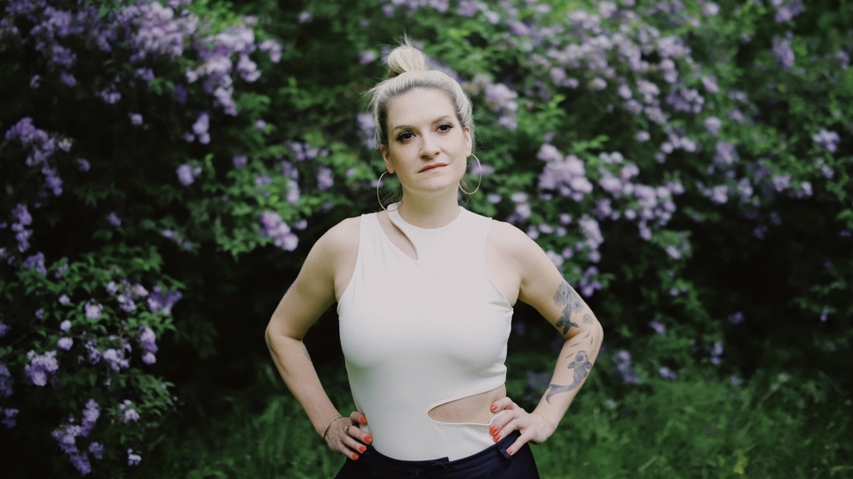 Photo of Amy Dabbs wearing a white vest in front of a purple flower bush