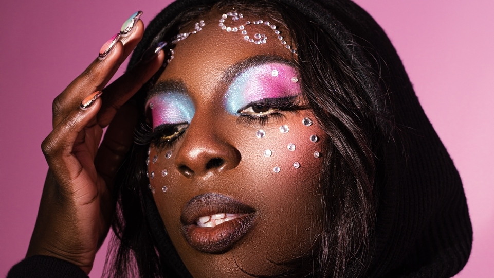 Photo of Anz wearing blue and pink sparkly eyeshadow in front of a pink background