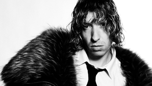 Daniel Avery in black and white looking at the camera in a big fur coat, white shirt and black tie