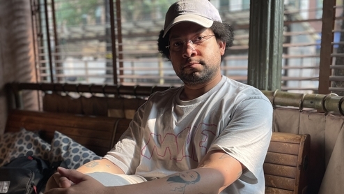 Photo of DJ Autopay sitting on a sofa while wearing a grey t-shirt and cream baseball cap