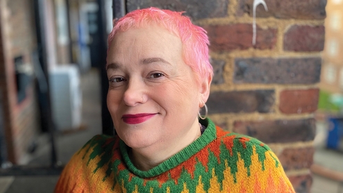 Jaye Ward with short cropped pink hair in a green, orange and yellow knitted sweater