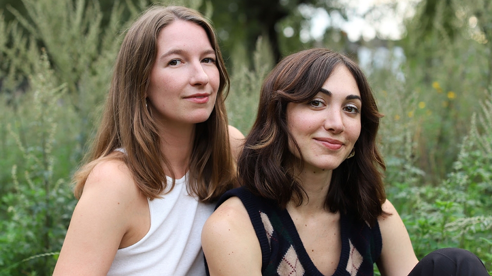 Rosie Ama and Nadia of Kiara Scuro sitting side by side in a field of tall grass and ferns