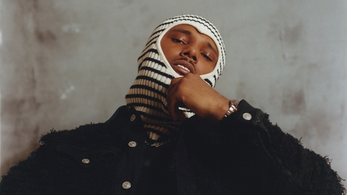 M1llionz in a knitted navy and cream balaclava in front of a concrete backdrop