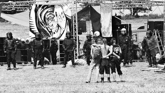 Black and white image by Molly Macindoe taken at a rave. Three ravers stand arm in arm while police block the decks