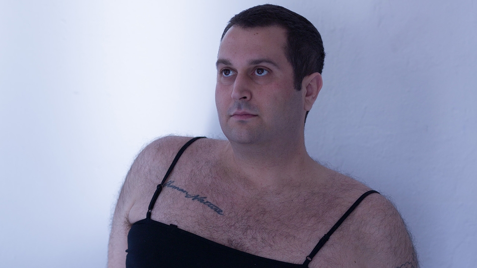 Press shot of Jorkes leaning against a wall. They're wearing a black vest 