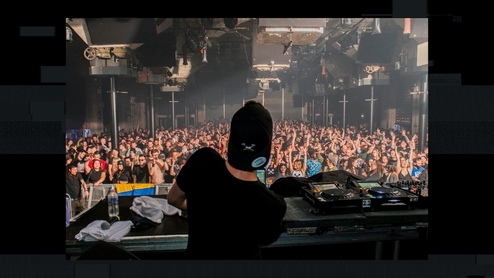 Photo taken from behind the DJ at a PRSPCT event. A large crowd is dancing in a warehouse space