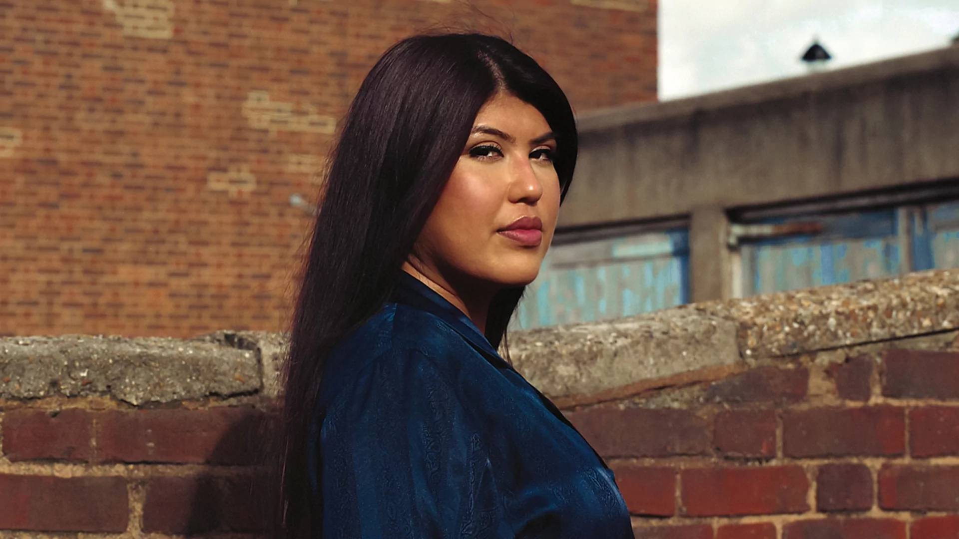 Fresha in a blue shirt against a red brick wall