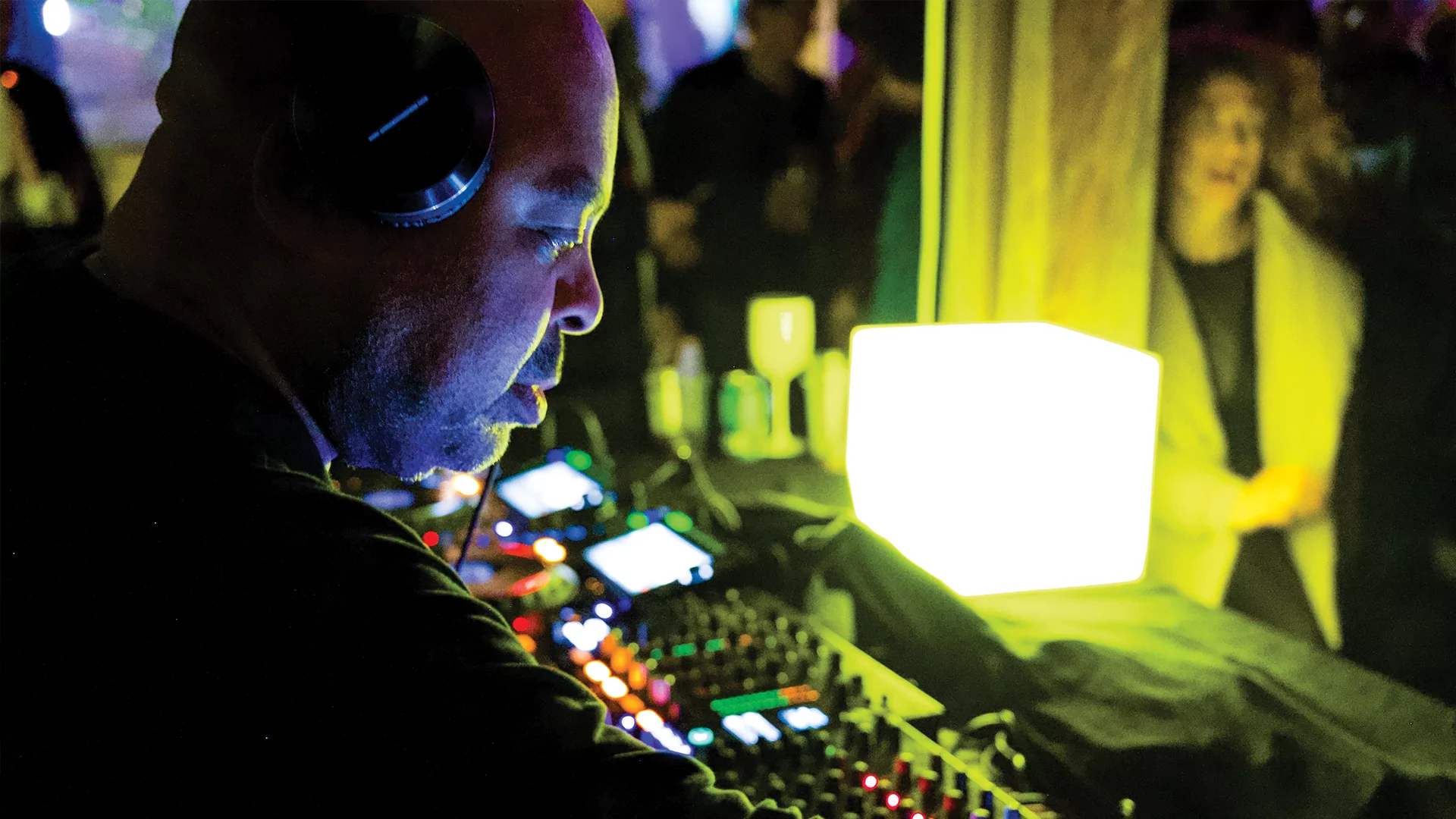 An over the shoulder photo of DJ Bone DJing in front of a yellow light