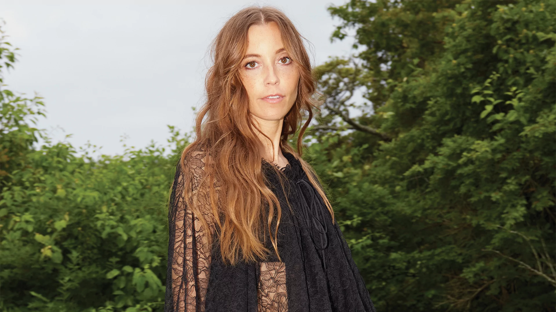 Photo of LP Giobbi wearing a long black dress and smiling against a backdrop of trees