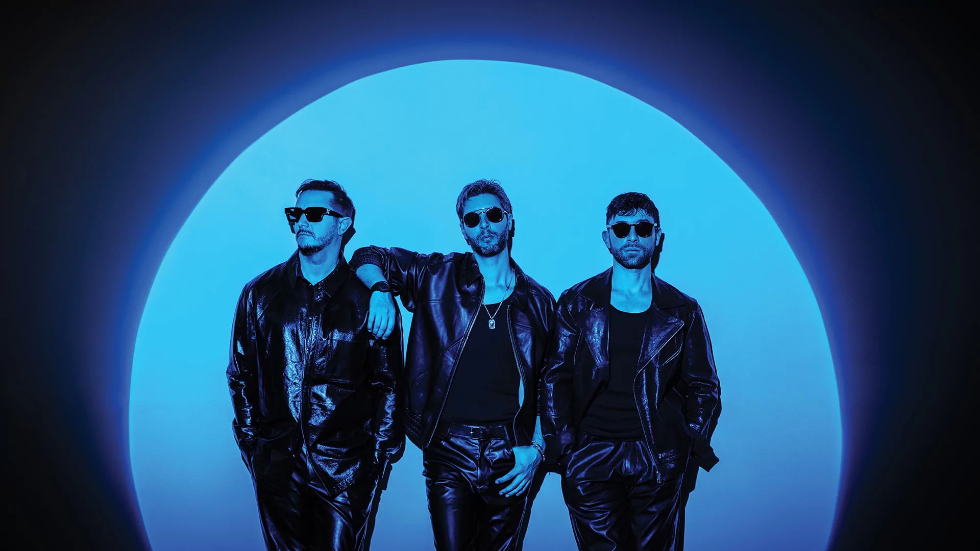 Photo of Meduza's Luca De Gregorio, Mattia Vitale and Simone Giani standing against a wall in a blue circular light