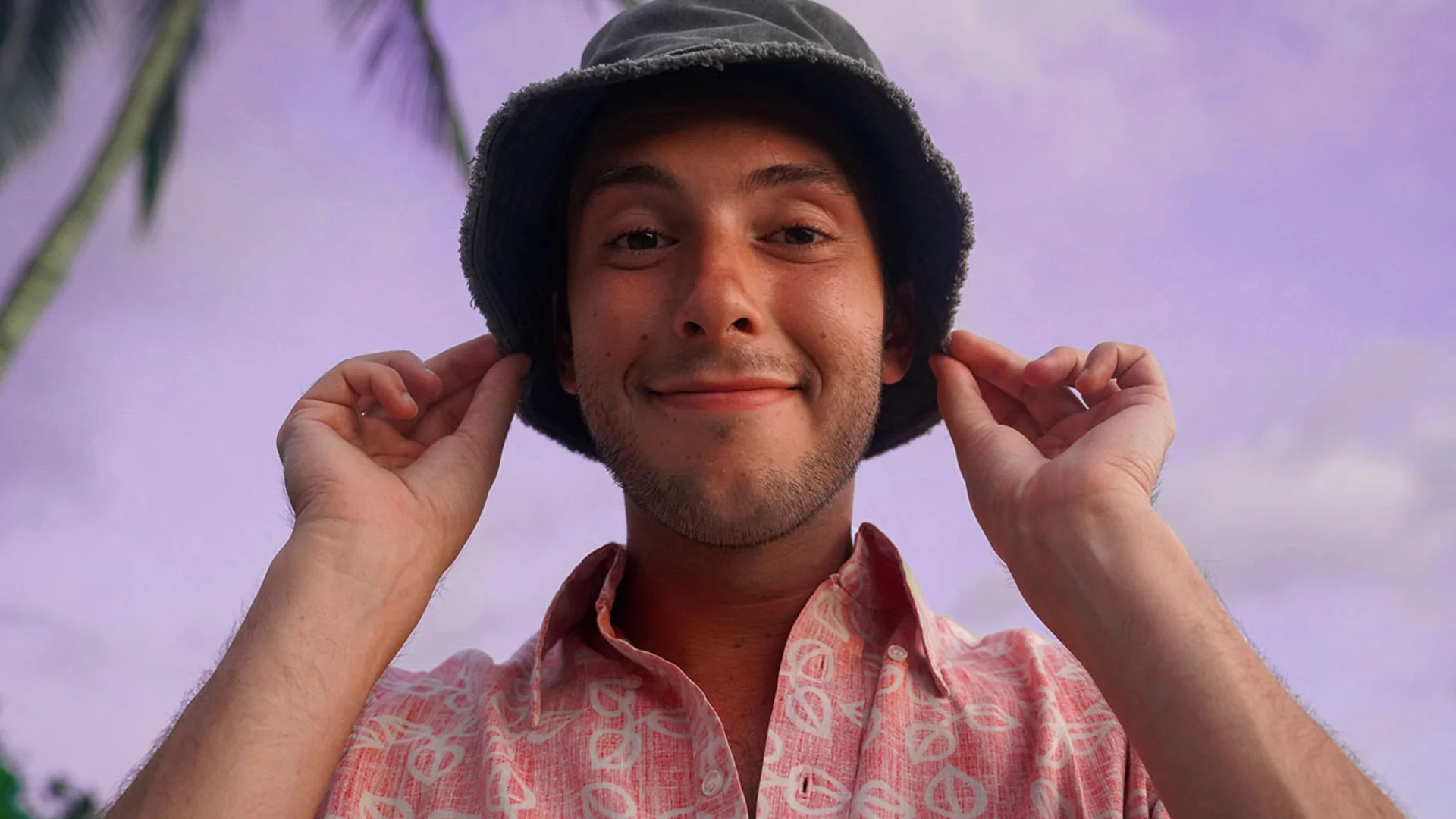 Press shot of Rodney Dinkles in a pink shirt, he's pulling a bucket hat over his ears