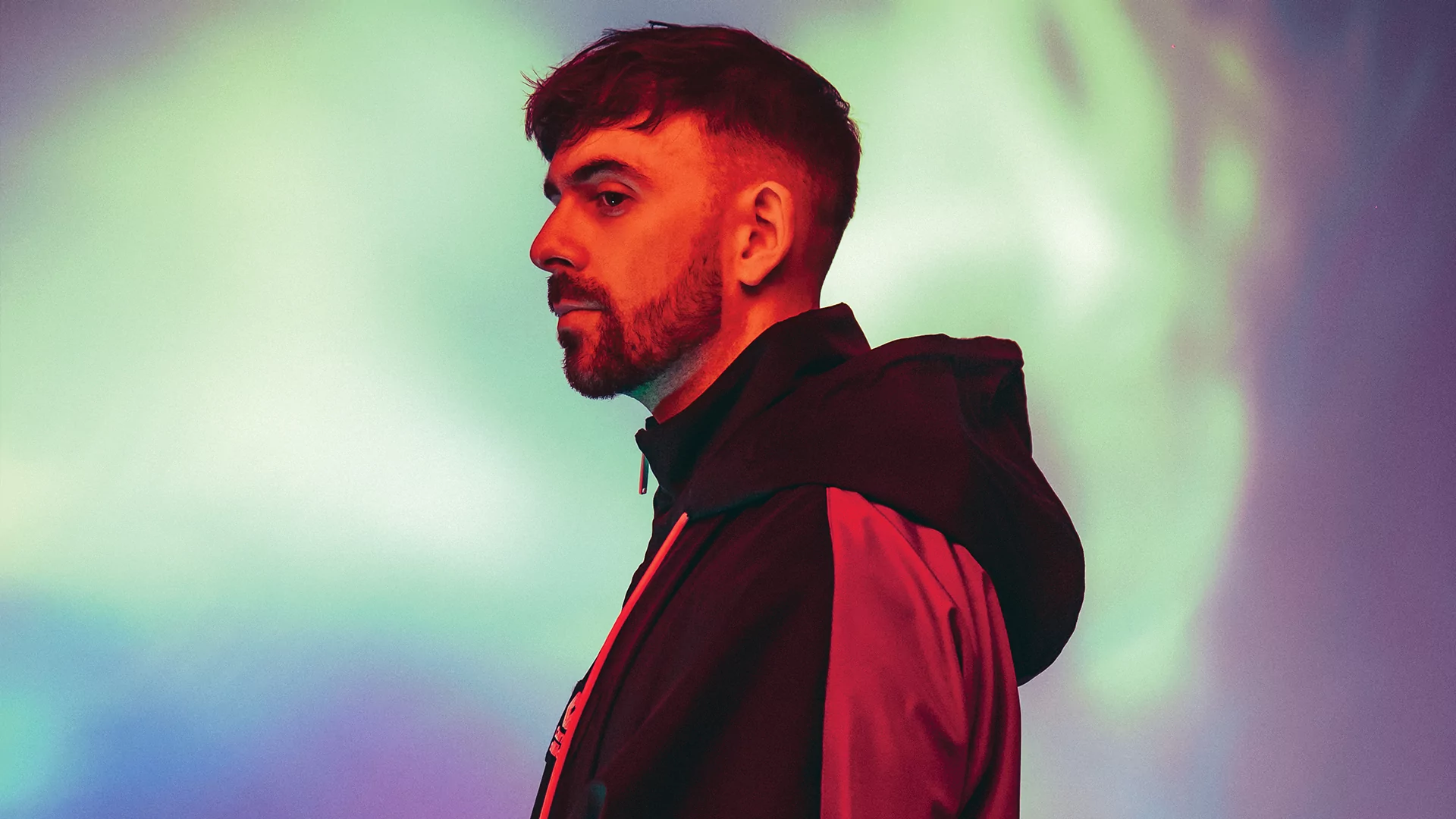 side profile portrait of patrick topping in a hooded jacket against a green and purple background