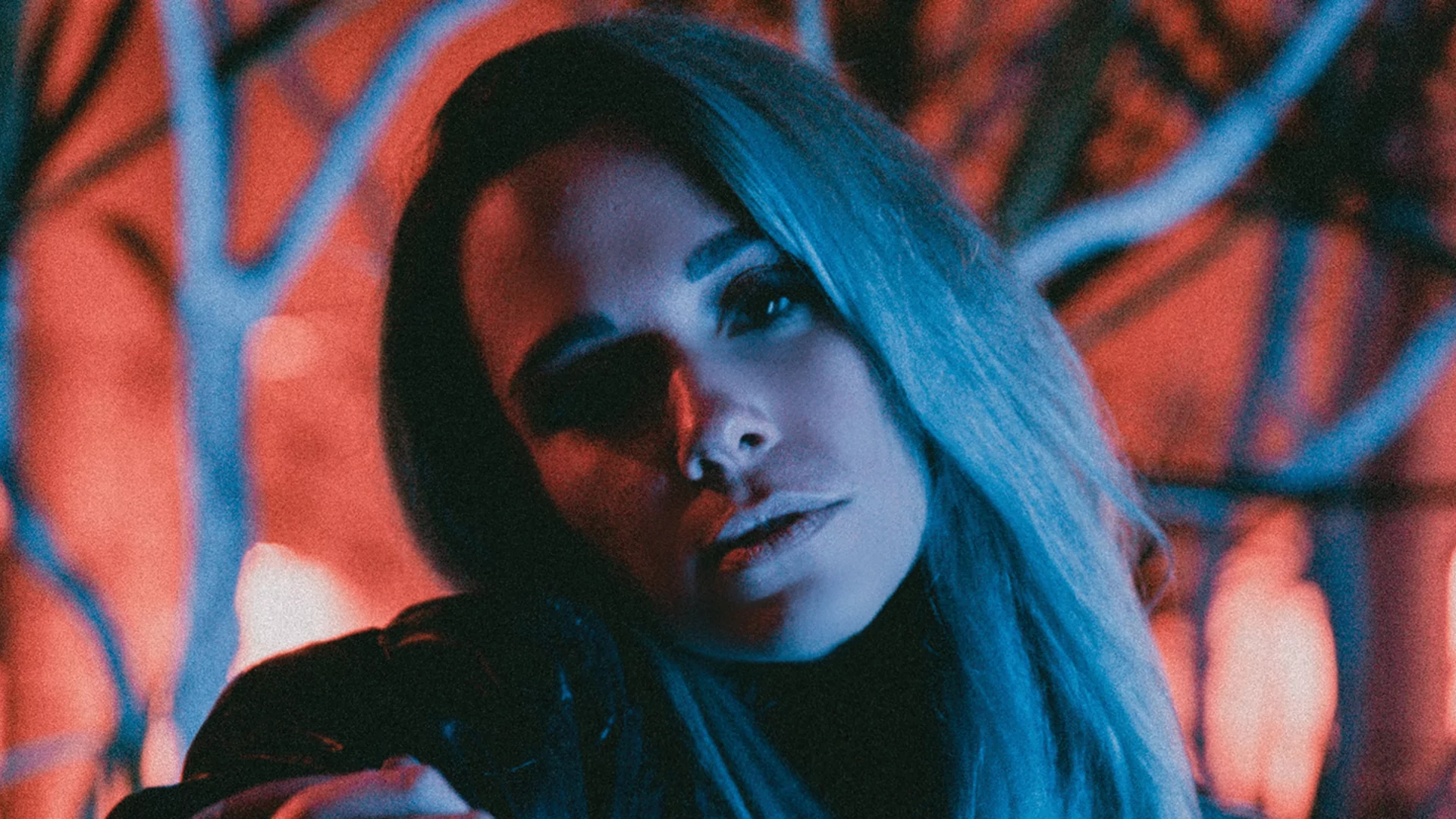 SKYLER under a pale blue light in front of a dusky red backdrop and trees